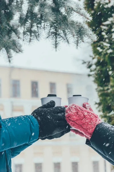 Обрізаний знімок пари, що тримає термопаузи з гарячими напоями на вулиці взимку — стокове фото