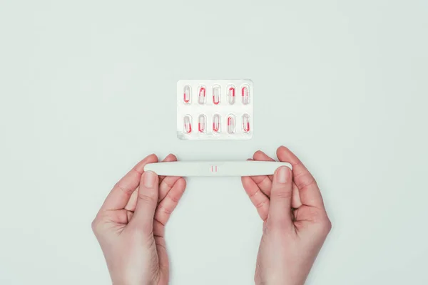 Partial view of woman holding pregnancy test in hands and contraceptive pills isolated on grey — Stock Photo