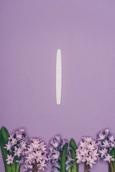 Top view of arranged flowers and pregnancy test isolated on purple — Stock Photo