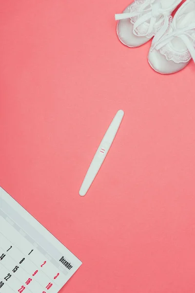 Top view of childish shoes, pregnancy test and calendar isolated on pink — Stock Photo