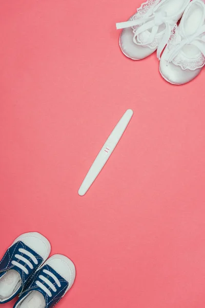 Vue de dessus de l'arrangement des chaussures enfantines et test de grossesse isolé sur rose — Photo de stock