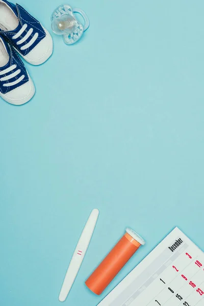 Vue du dessus des chaussures enfantines, sucette, calendrier, test de grossesse et contraceptif isolé sur bleu — Photo de stock