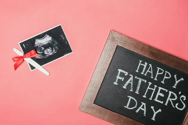 Top view of happy fathers day blackboard, ultrasound scan and pregnancy test with ribbon isolated on pink — Stock Photo