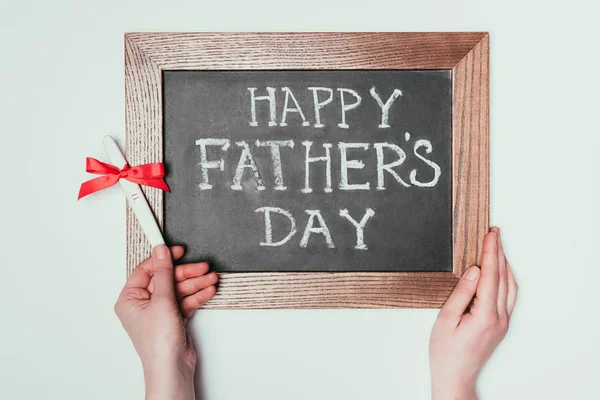 Cropped shot of woman holding pregnancy test with ribbon and happy fathers day lettering on blackboard isolated on grey — Stock Photo