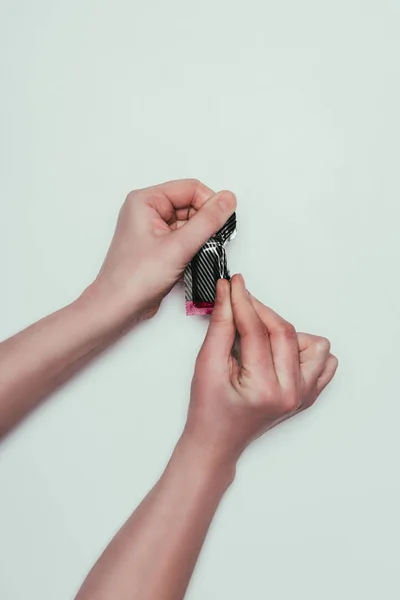 Partial view of woman opening condom isolated on grey — Stock Photo