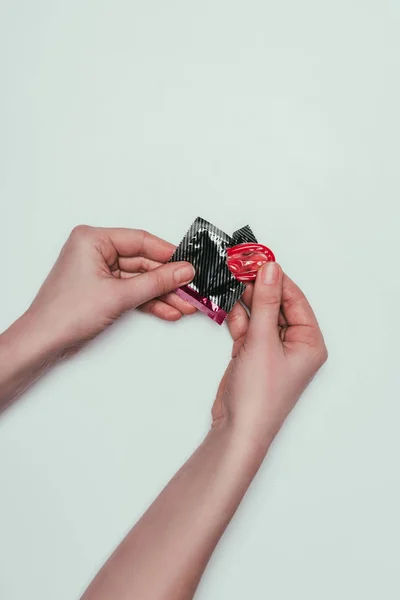 Partial view of woman opening condom isolated on grey — Stock Photo