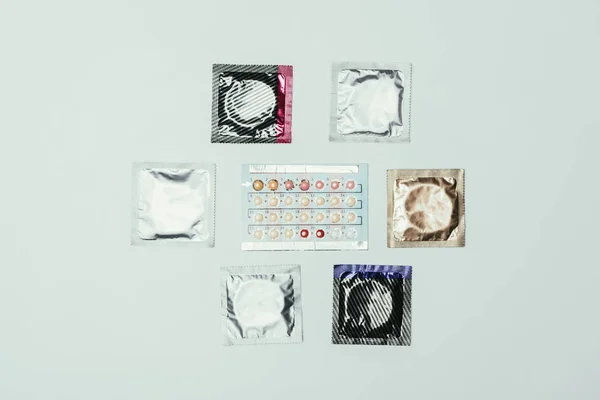 Vista superior de preservativos arranjados e pílulas contraceptivas isoladas em cinza — Fotografia de Stock