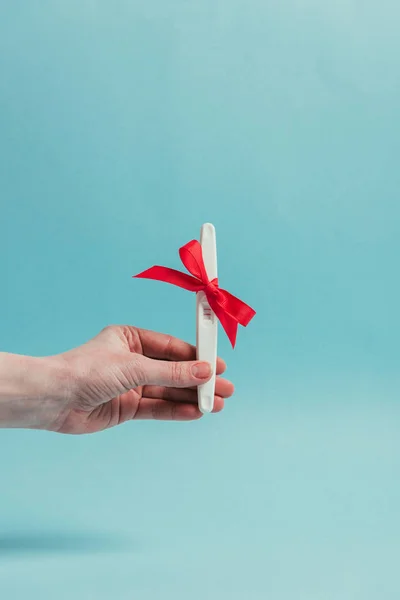 Cropped shot of woman holding pregnancy test with ribbon isolated on blue — Stock Photo