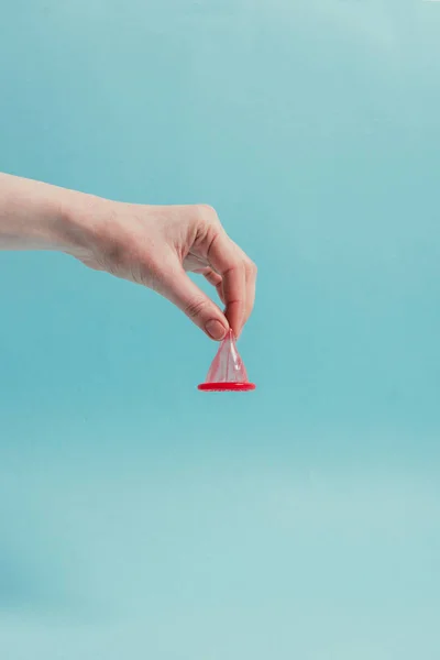 Partial view of woman holding opened condom in hand isolated on blue — Stock Photo