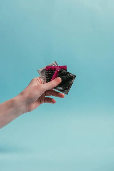 Tiro recortado de mujer sosteniendo condones en la mano aislado en azul - foto de stock