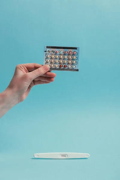 Partial view of woman with contraceptive pills in hand and pregnancy test isolated on blue — Stock Photo