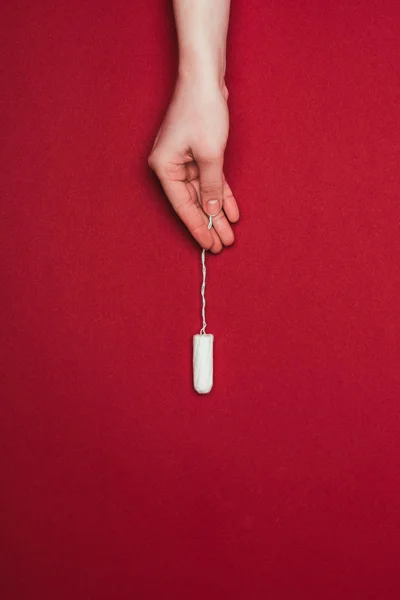 Cropped shot of woman holding tampon in hand isolated on red — Stock Photo