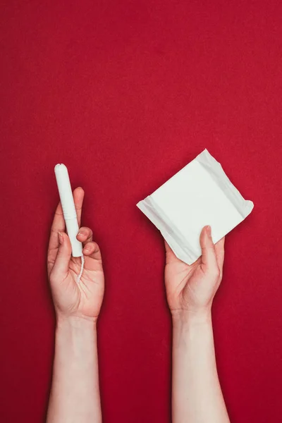 Abgeschnittene Aufnahme einer Frau mit Menstruationspolster und Tampon isoliert auf Rot — Stockfoto