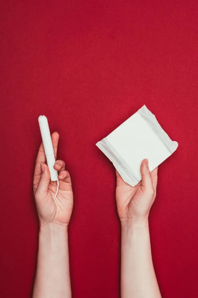 Tiro cortado de mulher segurando almofada menstrual e tampão isolado em vermelho — Fotografia de Stock