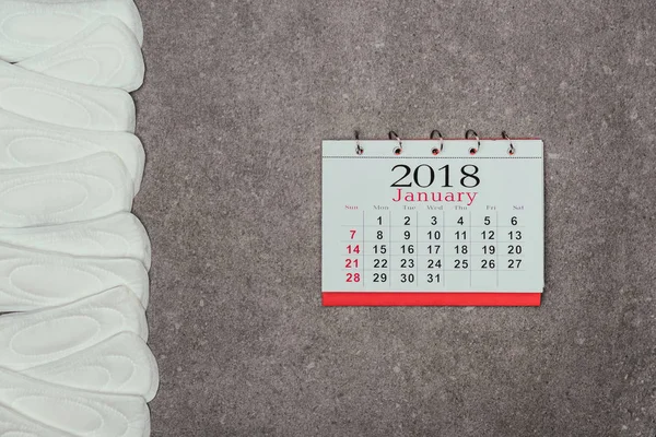 Vista dall'alto di pastiglie mestruali disposte e calendario sulla superficie grigia — Foto stock