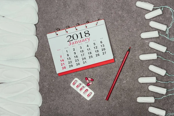 Верхний вид устроенных менструальных прокладок и тампонов, календарь и таблетки на серой поверхности — стоковое фото