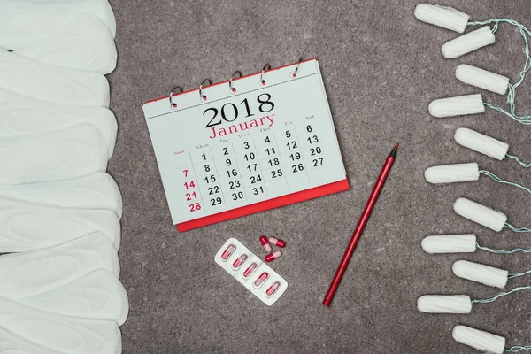 Vista superior de almofadas e tampões menstruais arranjados, calendário e comprimidos na superfície cinzenta — Fotografia de Stock