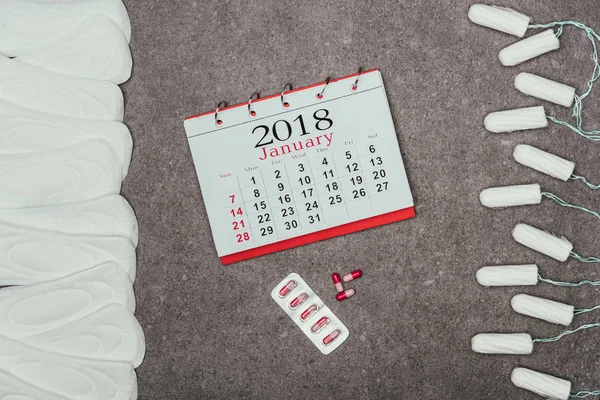 Top view of arranged menstrual pads and tampons, calendar and pills on grey surface — Stock Photo