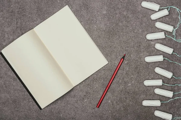 Draufsicht auf leeres Notizbuch, Marker und Menstruationstampons auf grauer Oberfläche — Stockfoto