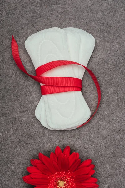 Top view of arranged menstrual pads with ribbon and red flower on grey surface — Stock Photo