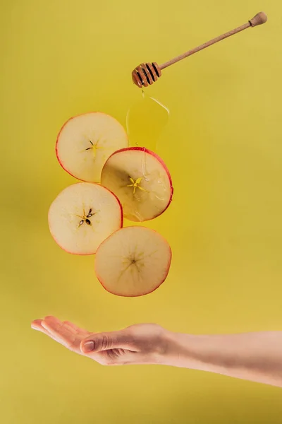 Partial view of female hand and levitating pieces of apple with honey — Stock Photo