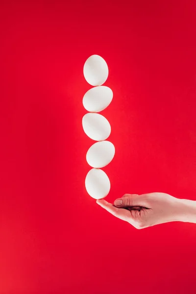 Partial view of woman holding levitating raw chicken eggs on finger isolated on red — Stock Photo