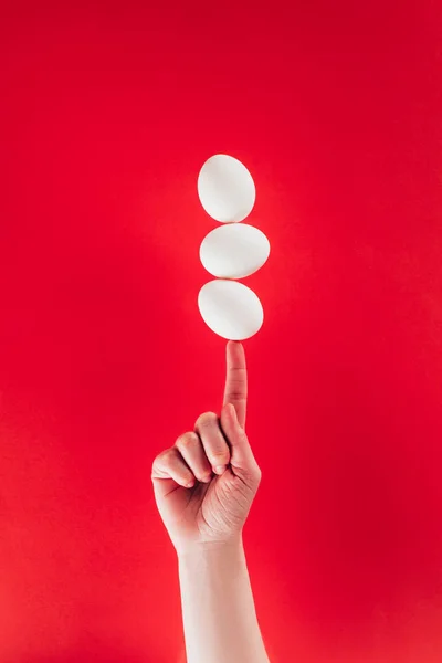 Partial view of woman holding levitating raw chicken eggs on finger isolated on red — Stock Photo