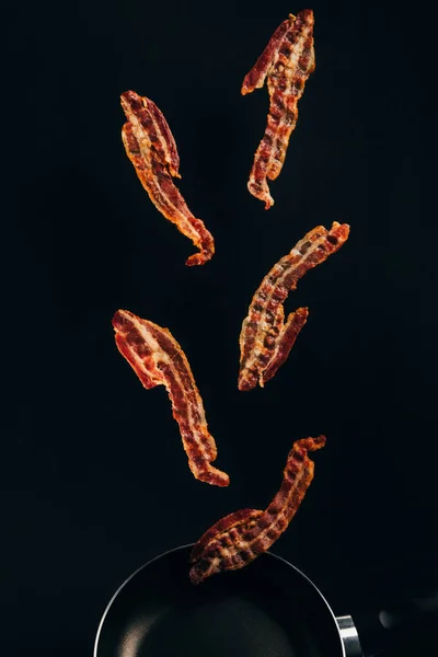 Close up view of pieces of bacon falling on frying pan isolated on black — Stock Photo