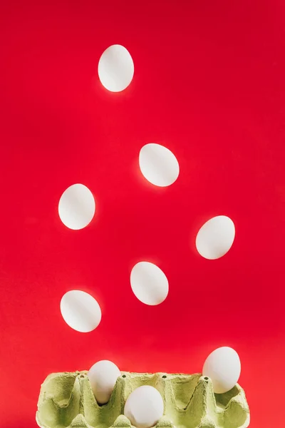 Close up view of levitating raw chicken eggs and cardboard egg box isolated on red — Stock Photo