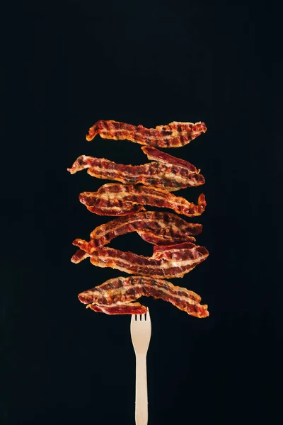 Close up view of pieces of bacon on fork isolated on black — Stock Photo