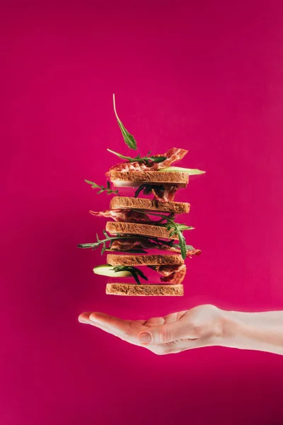 Vue partielle de la main féminine et des sandwichs lévitants isolés sur rose — Photo de stock