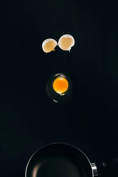 Close up view of raw egg yolk falling on frying pan isolated on black — Stock Photo