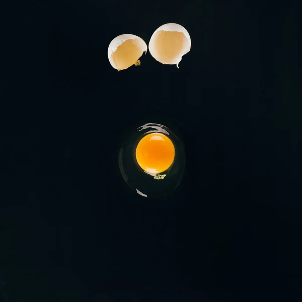 Close up view of raw egg yolk falling on frying pan isolated on black — Stock Photo