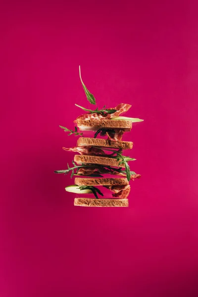 Закрытый вид на левитационные бутерброды с кусочками бекона и аругулой, изолированные на розовом фоне — стоковое фото