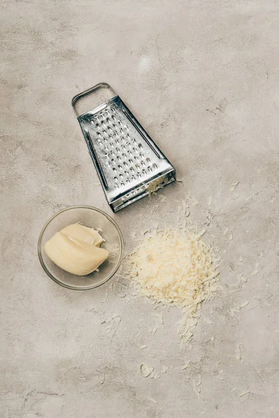 Rallador y trozo de queso en tazón sobre fondo claro - foto de stock