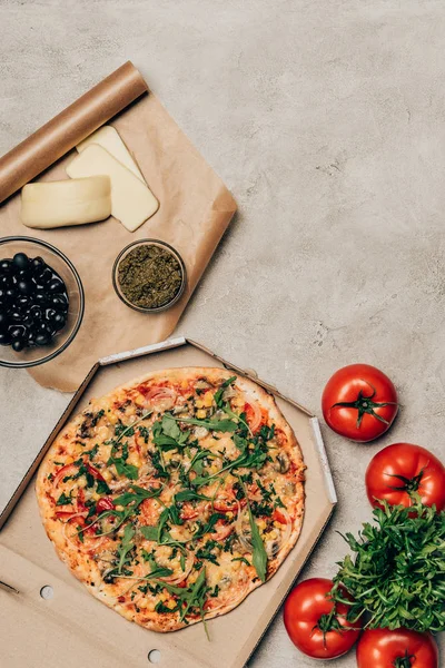 Whole pizza in cardboard box with tomatoes, cheese and olives on light background — Stock Photo