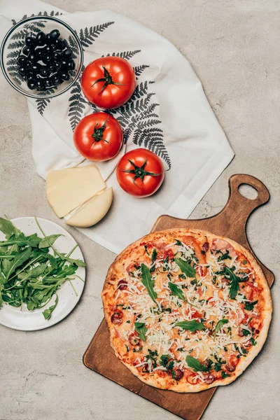 Delicious pizza on wooden cutting board and recipe ingredients on light background — Stock Photo