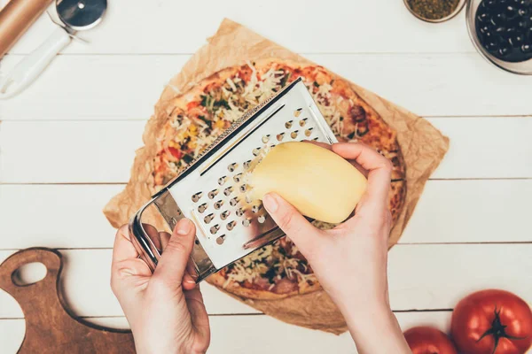 Vue rapprochée du fromage râpé femme sur pizza sur fond de bois blanc — Photo de stock