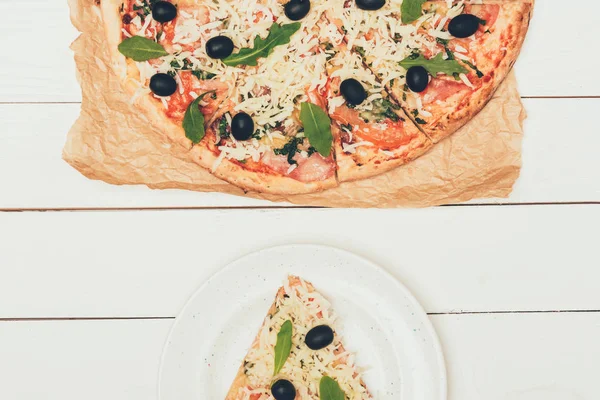 Tranche de pizza et pizza entière sur fond de bois blanc — Photo de stock