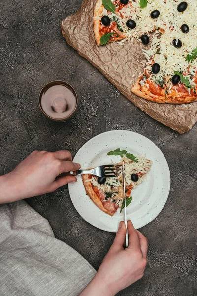 Nahaufnahme einer Frau, die ein Stück Pizza auf dunklem Hintergrund schneidet — Stockfoto