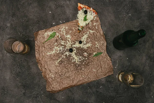 Pizza leftovers on craft paper with beer on dark background — Stock Photo