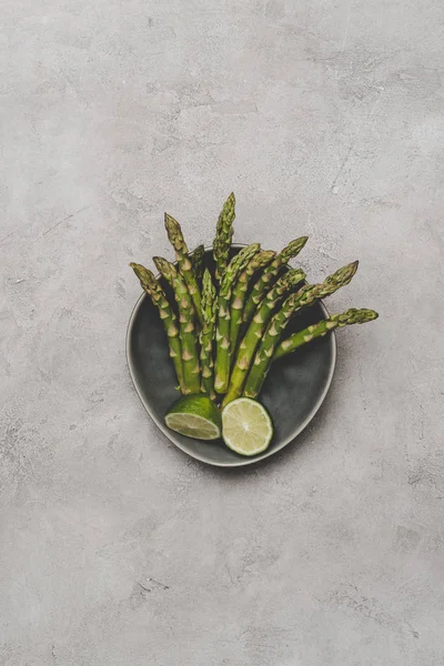 Draufsicht auf frischen gesunden Spargel und Limettenscheiben auf Teller auf grau — Stockfoto