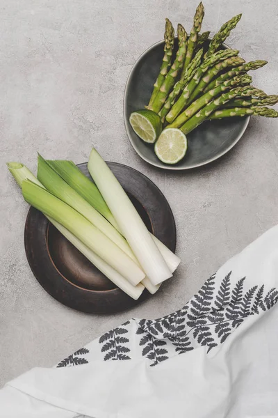 Vue de dessus des poireaux frais sains, des asperges et du citron vert sur des assiettes — Photo de stock