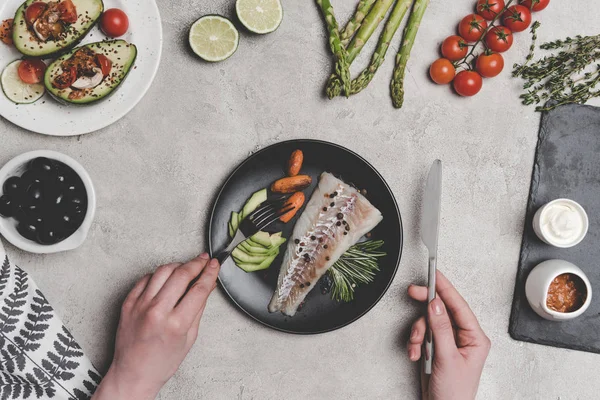 Tiro recortado de la persona que come pescado con verduras saludables en gris - foto de stock