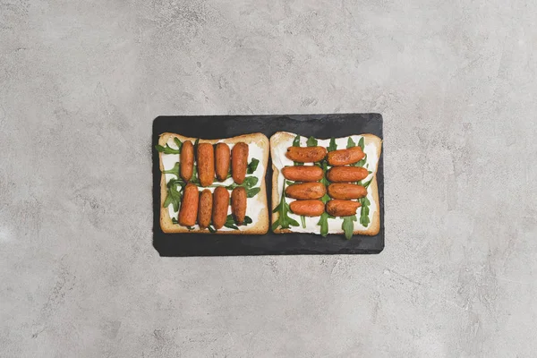 Vista superior de sanduíches saudáveis saborosos com arugula e cenouras de bebê no quadro de ardósia — Fotografia de Stock