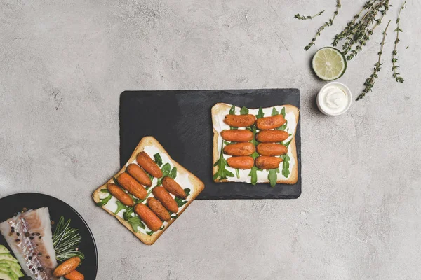 Vista superior de sándwiches saludables con zanahorias bebé y rúcula en pizarra - foto de stock