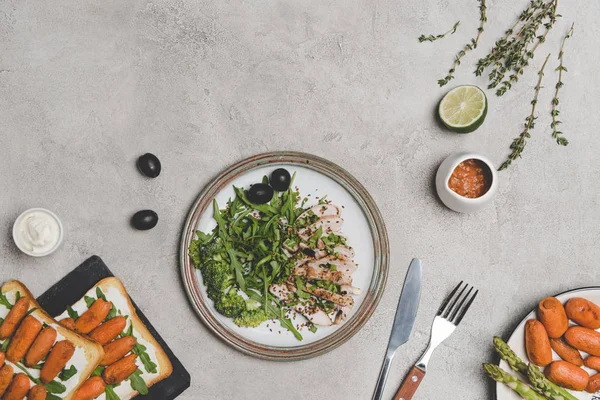 Vue du dessus de la viande tranchée avec des légumes frais et des sandwichs avec des bébés carottes sur gris — Photo de stock