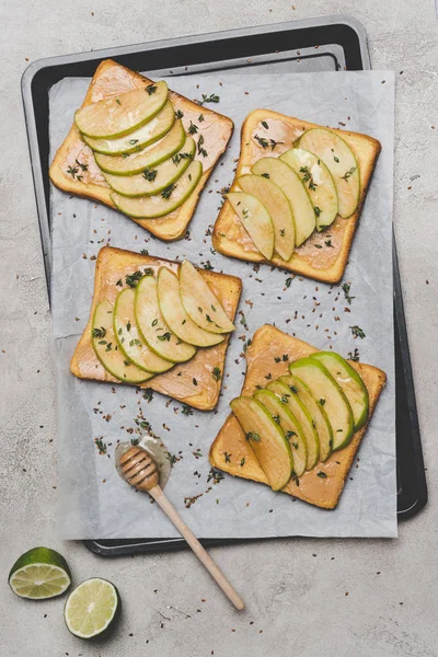 Healthy sandwiches with slices of apple, lime and honey dipper on grey — Stock Photo