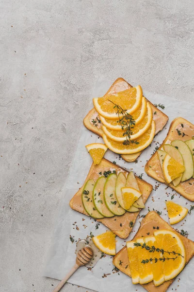 Top view of healthy sandwiches with slices of apple and orange and honey dipper on grey — Stock Photo