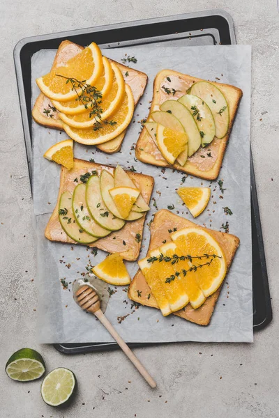 Healthy sandwiches with slices of apple and orange, lime and honey dipper on grey — Stock Photo
